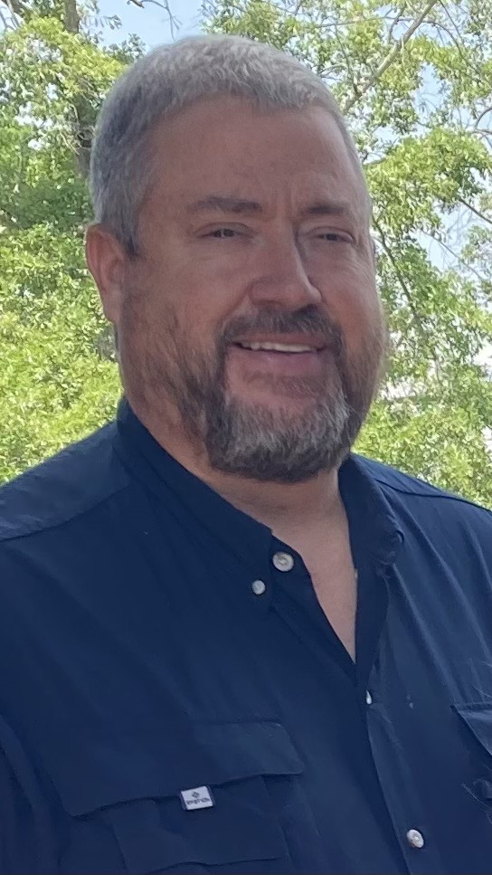 Smiling bearded man outdoors with green trees